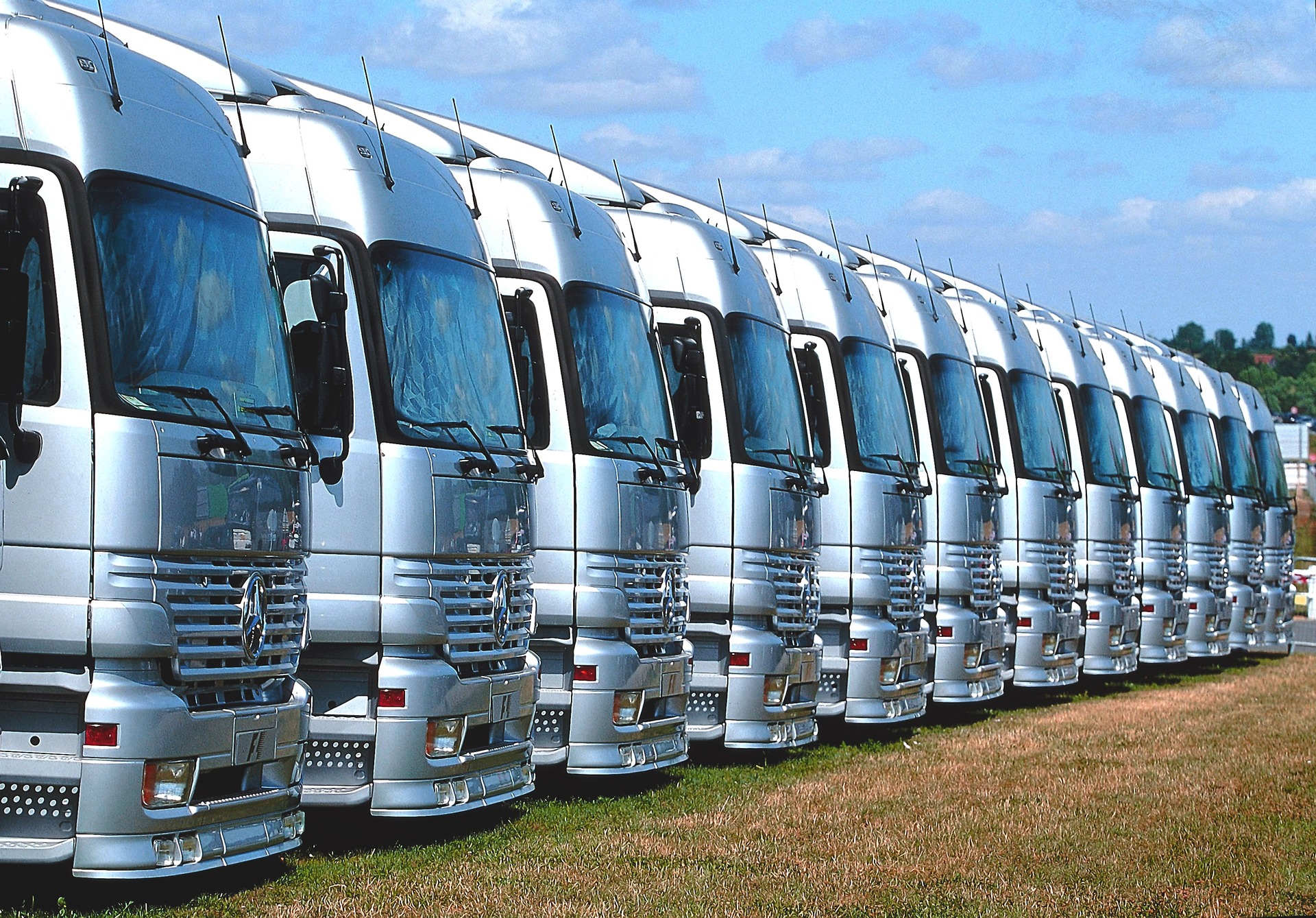 Reihe von silbernen LKWs, die geparkt auf einer Wiese stehen, bereit für den Einsatz.