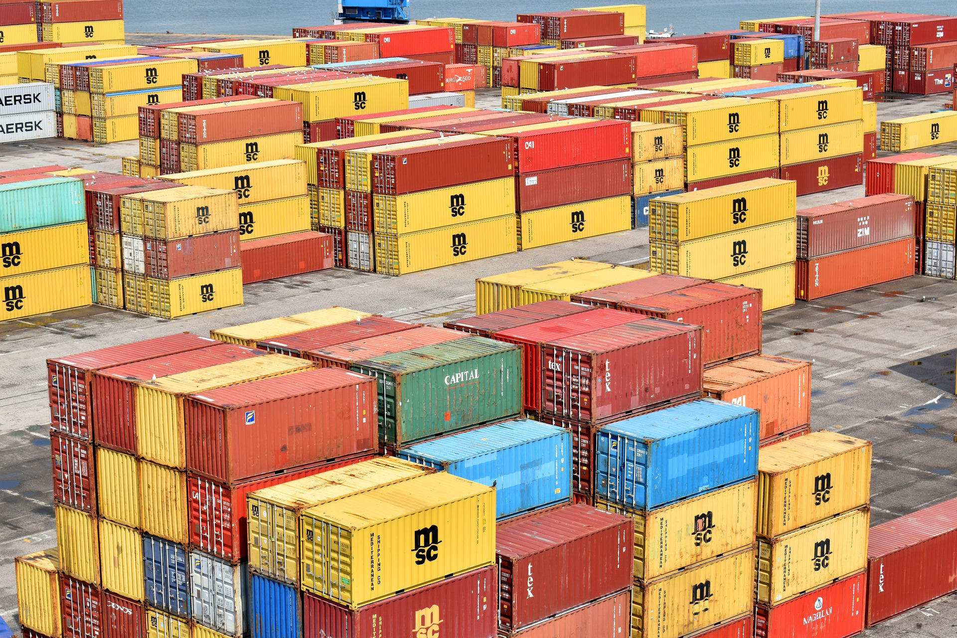 Containerstapel in verschiedenen Farben, organisiert auf einem Hafenplatz, bereit für den Transport auf Schiffen.